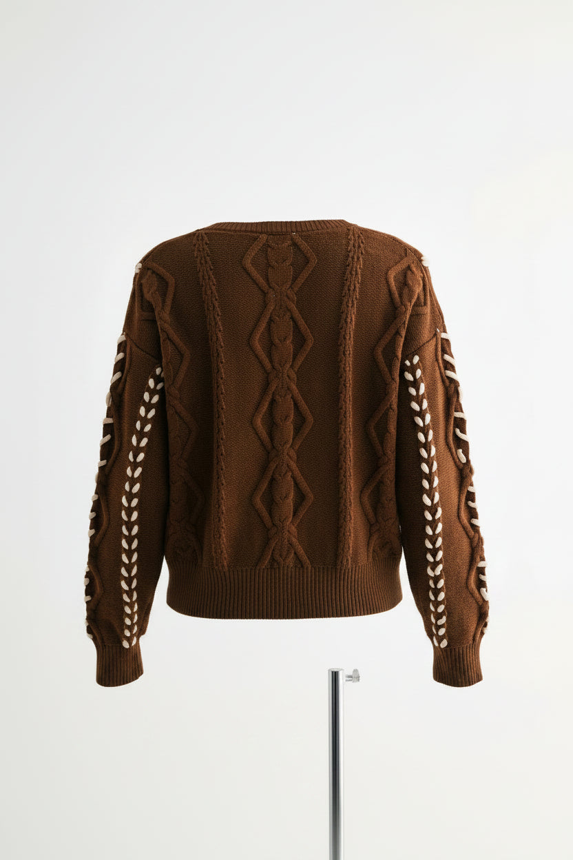 shown from the back wearing a brown cable-knit sweater with cream braided sleeve details.
