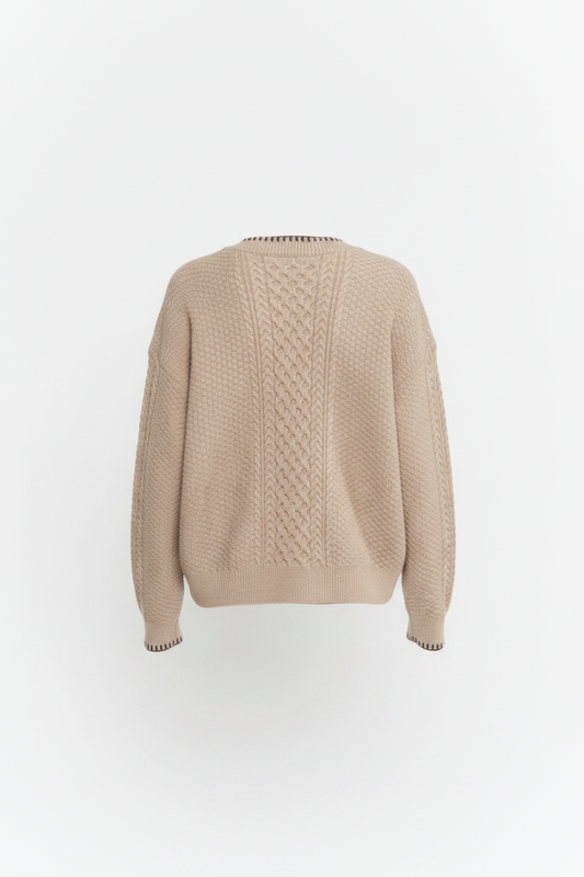 A woman shown from the back wearing a beige cable-knit sweater and dark brown pants against a plain white studio background.
