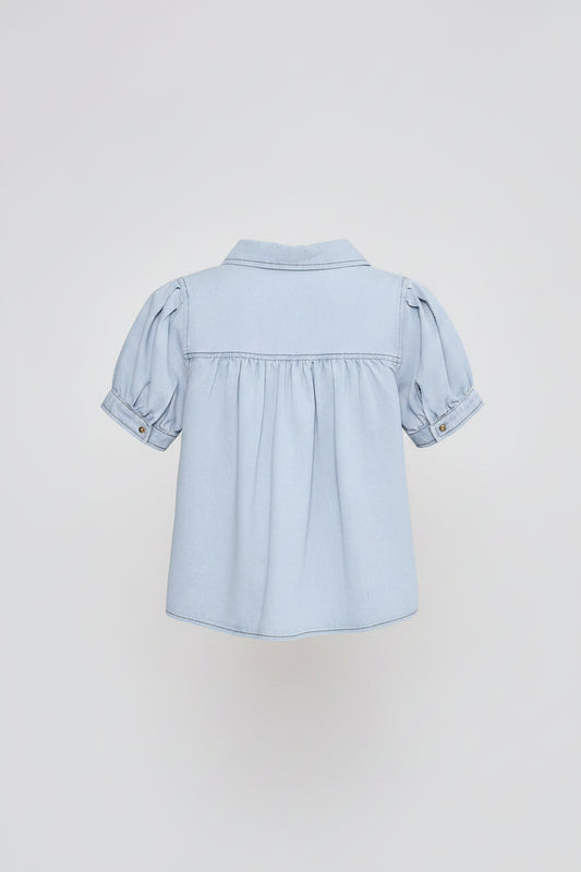 A woman shown from the back wearing a light blue cropped short-sleeve blouse with puffed sleeves and white wide-leg pants, against a plain light gray studio background.