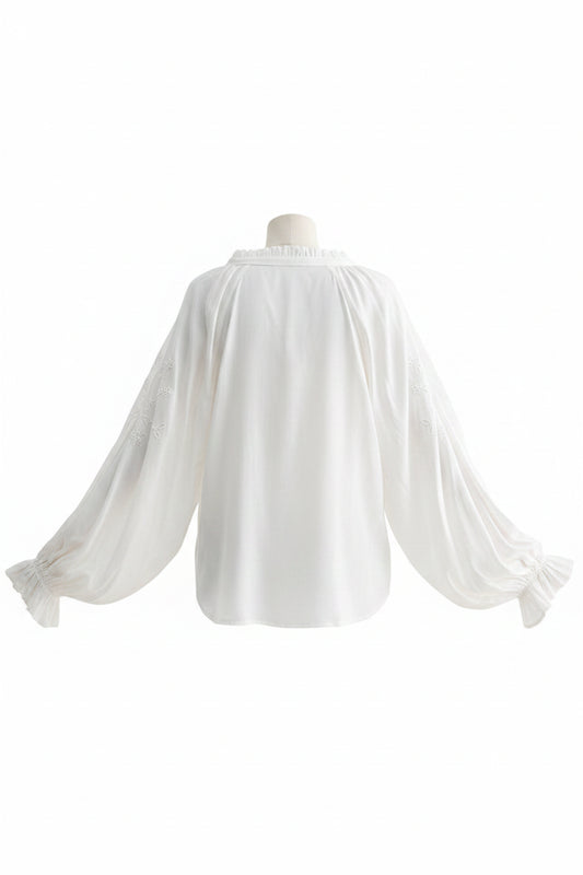 Woman wearing a white blouse with sheer sleeves and blue jeans on a white background