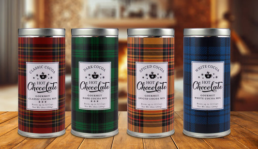 Four plaid hot chocolate tins in classic, dark, spiced, and white cocoa varieties displayed on a wooden table