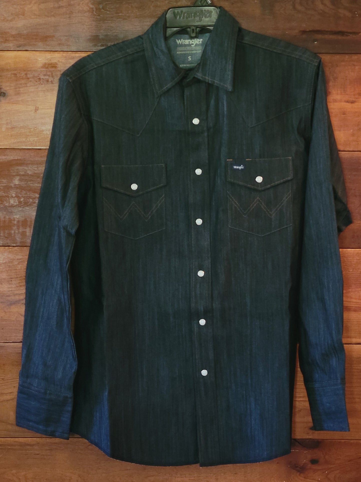 Dark denim shirt with white buttons on a wooden surface