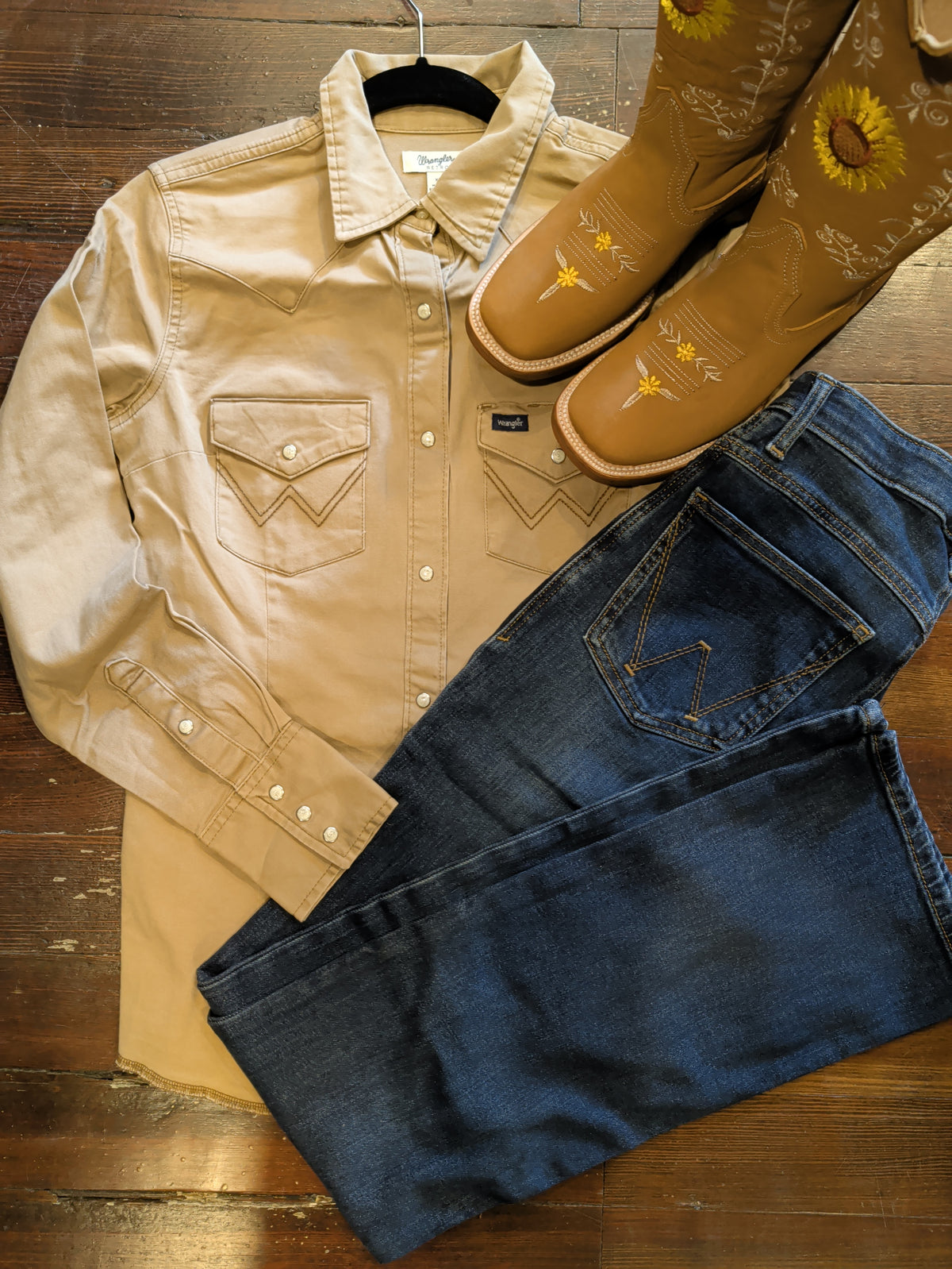 Overhead outfit arrangement with Wrangler Rawhide snap shirt, dark jeans and sunflower-embroidered tan boots.
