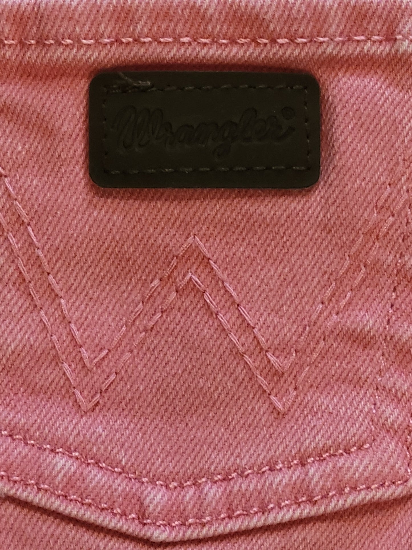 Close-up of a pink fabric with a black label featuring Wrangler logo.