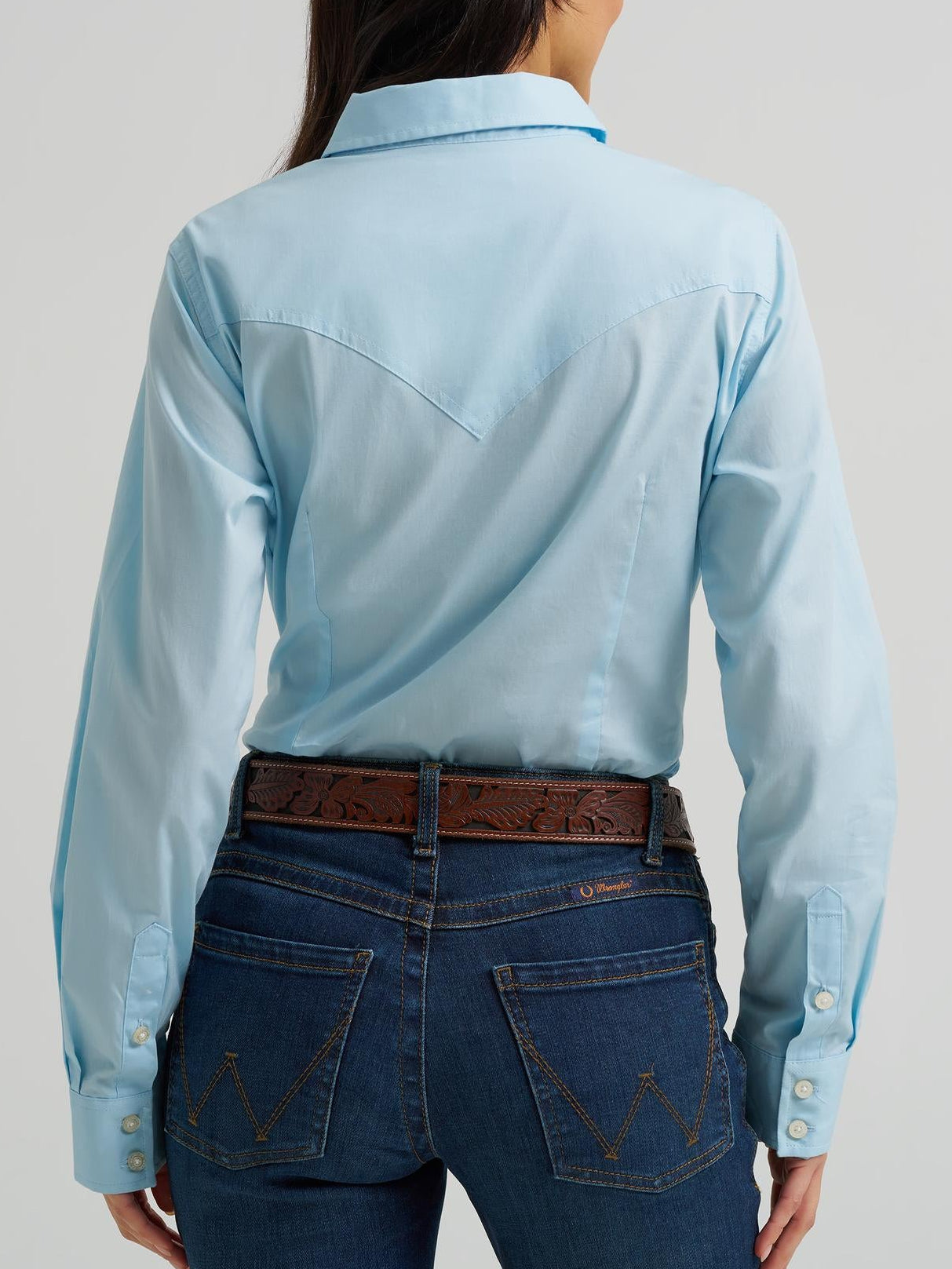Person wearing a light blue shirt and dark blue jeans on a plain background