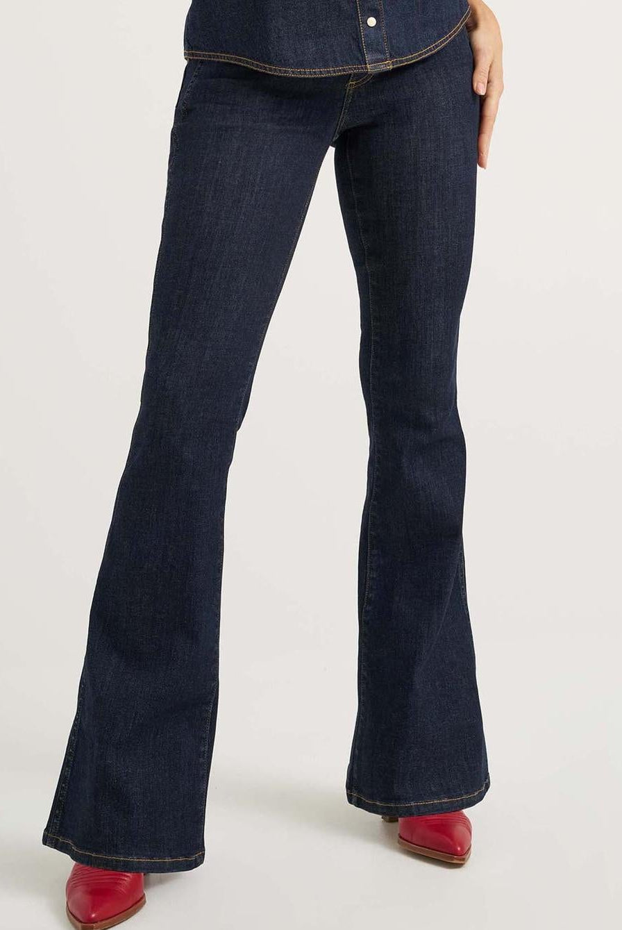 Woman wearing a sleeveless denim top with floral embroidery and flared jeans on a white background