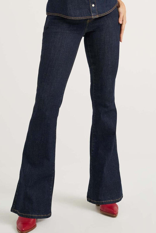 Woman wearing a sleeveless denim top with floral embroidery and flared jeans on a white background