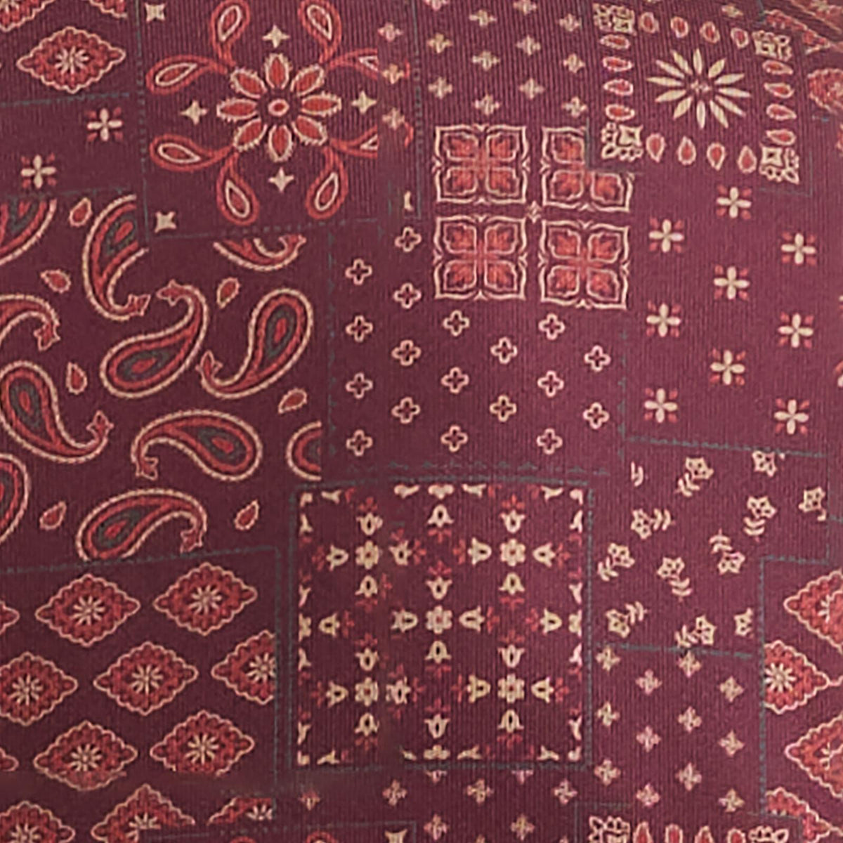 Close-up of the Fig Patchwork Bandana print showing burgundy, paisley, floral, and geometric motifs on the ATG x Wrangler polo.