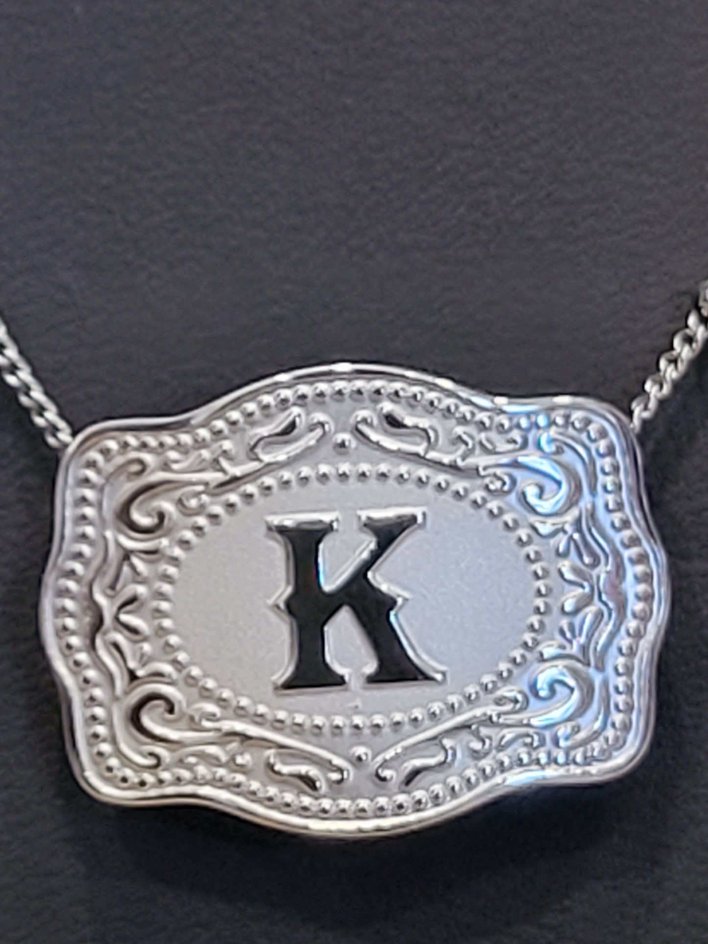 Decorative silver pendant with a black symbol on a dark background