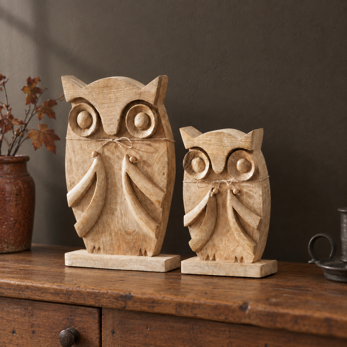 Large and small carved mango wood owls with twine bows displayed on a rustic console, sold individually