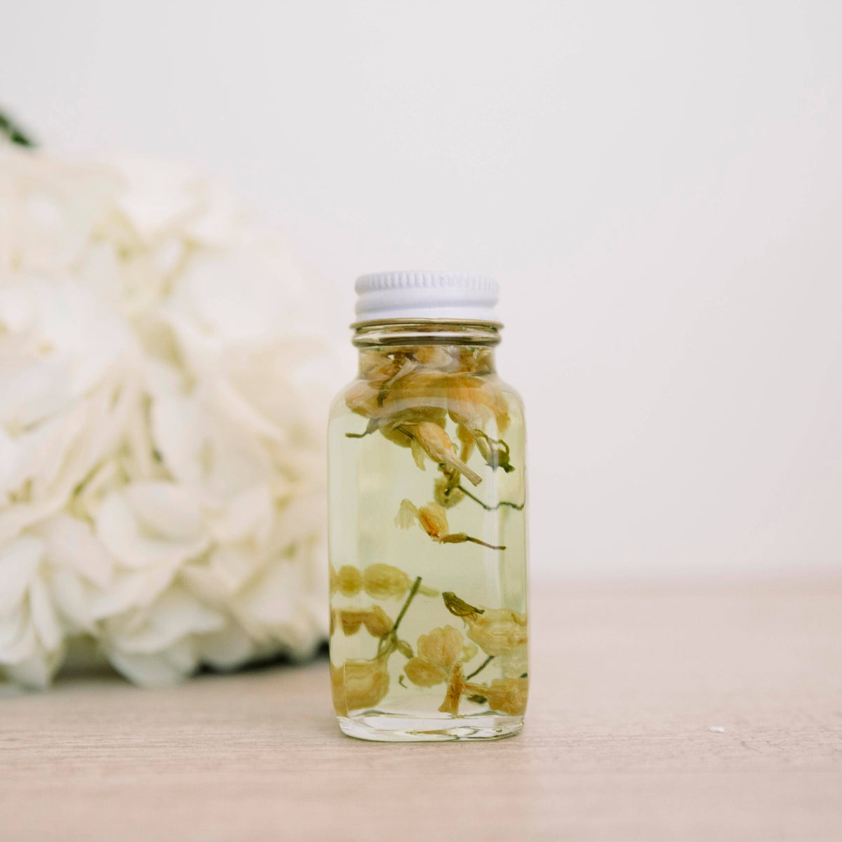 Glass bath oil bottle containing pale blossoms beside white flowers