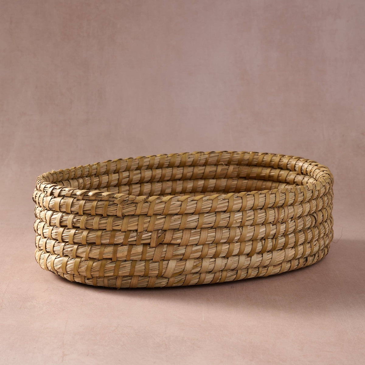 Side view of the Gama Oval Leaf Bread Warmer showing the natural tan woven kaisa grass basket