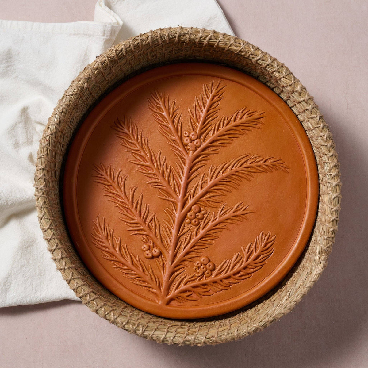 RoseMerry Bread Warmer viewed from above, with a botanical-patterned terracotta stone inside a round woven basket