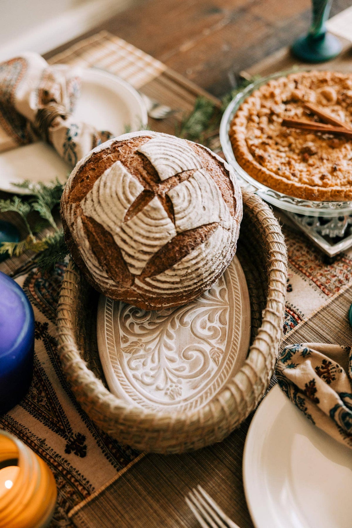 Toasty Bread Basket holding a round loaf on a dining table beside a pie and place settings