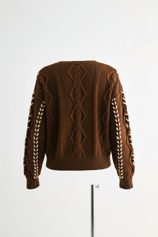  shown from the back wearing a brown cable-knit sweater with cream braided sleeve details.