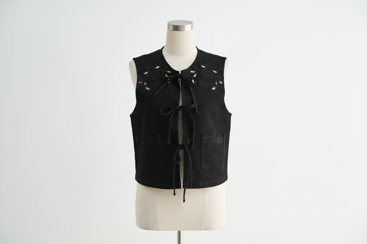  black sleeveless top with cut-out details and white pants on a light gray background