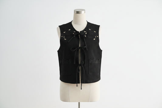  black sleeveless top with cut-out details and white pants on a light gray background
