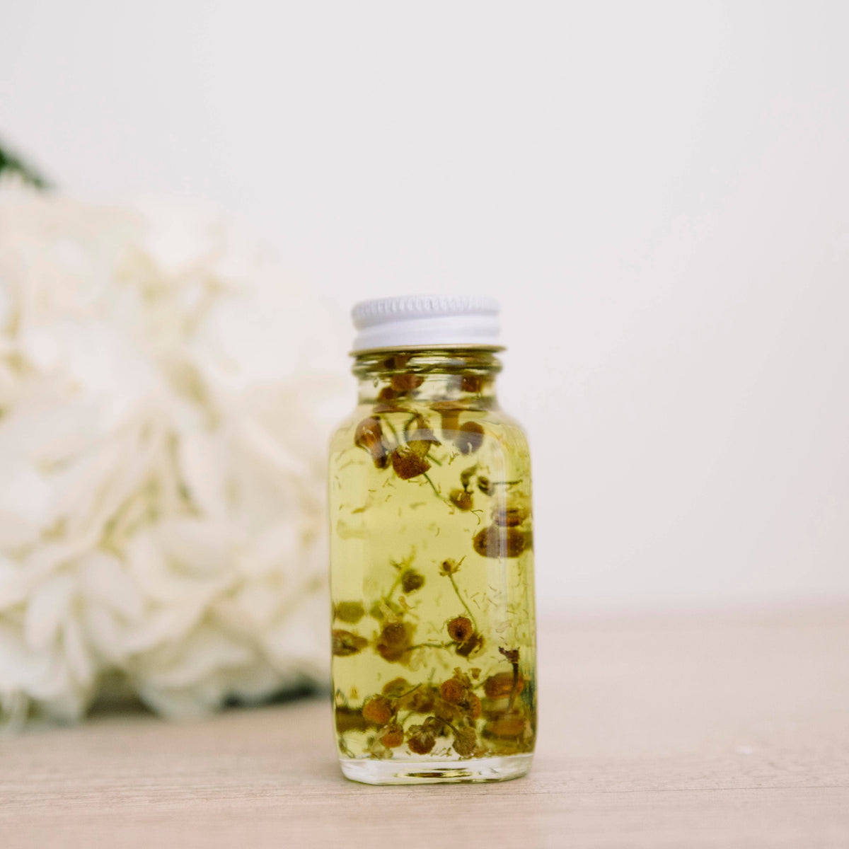 Glass bath oil bottle containing small yellow flower heads beside white flowers