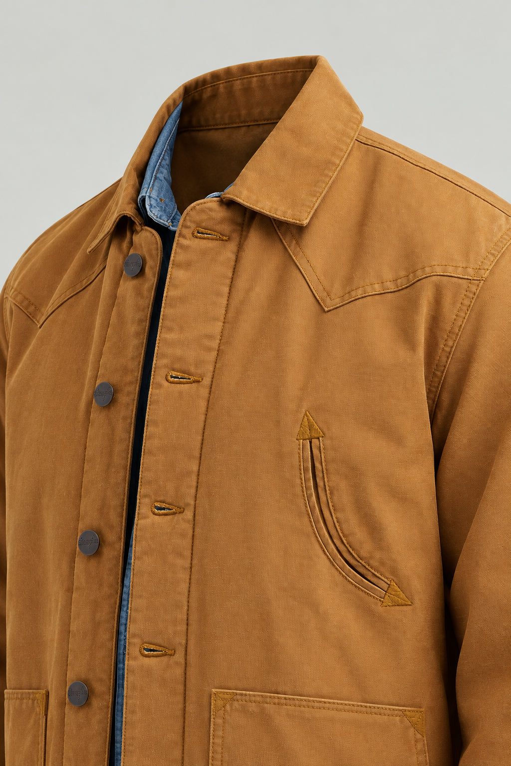 Close-up of a tan work jacket over a blue shirt, showing the collar, front buttons, and chest pocket.