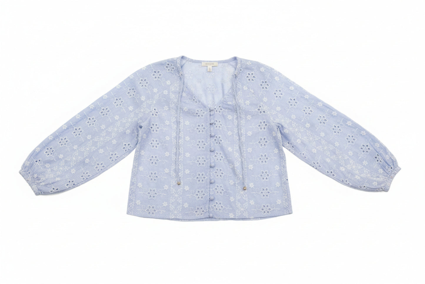 Woman wearing a light blue floral blouse and denim shorts outdoors.
