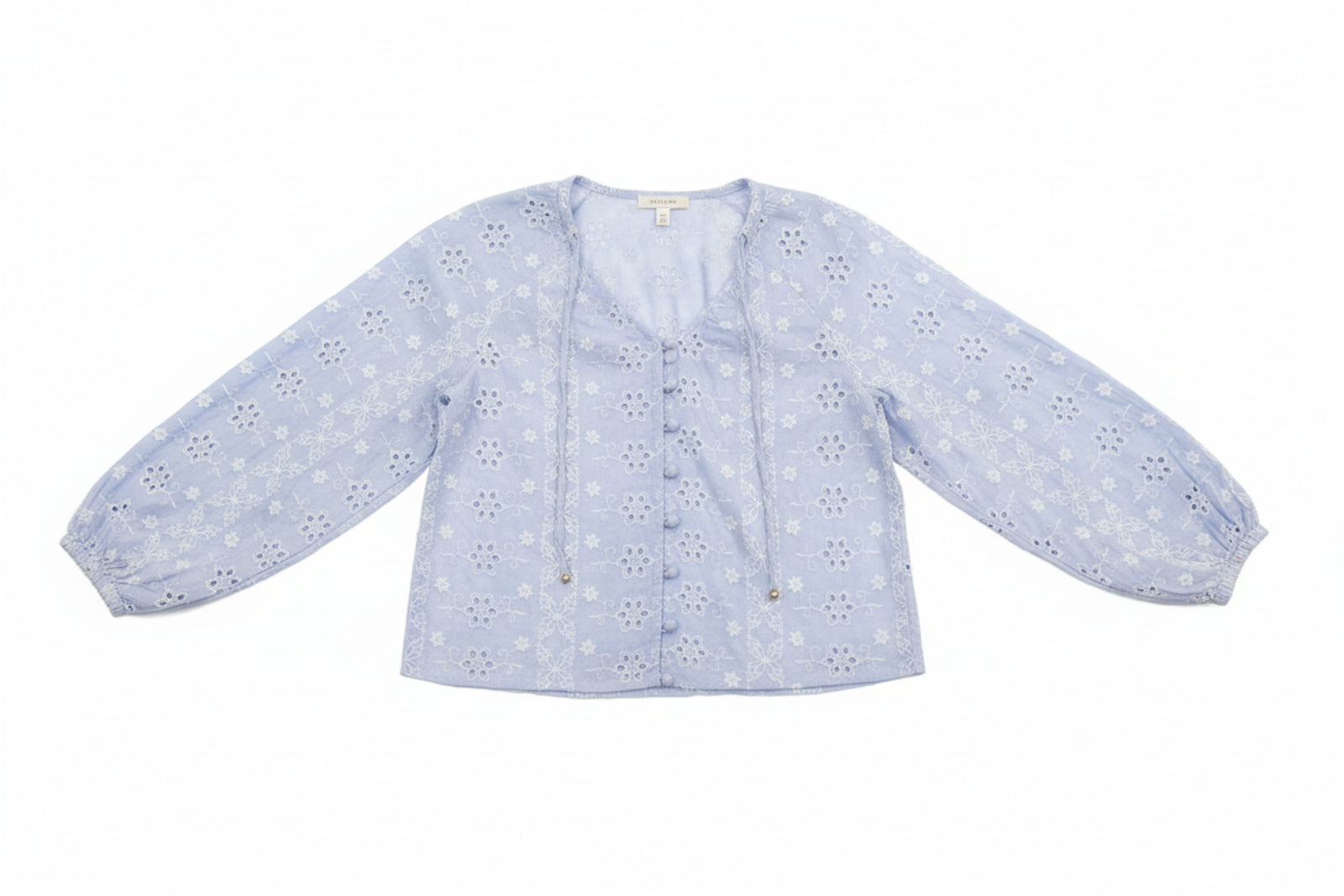 Woman wearing a light blue floral blouse and denim shorts outdoors.
