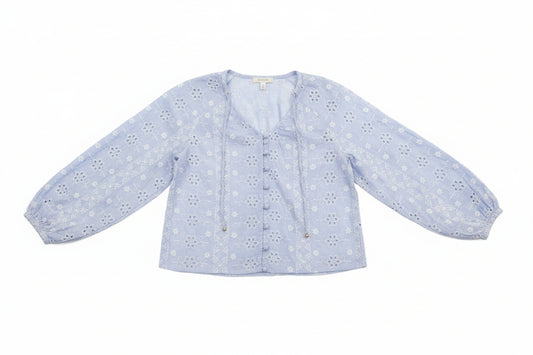 Woman wearing a light blue floral blouse and denim shorts outdoors.