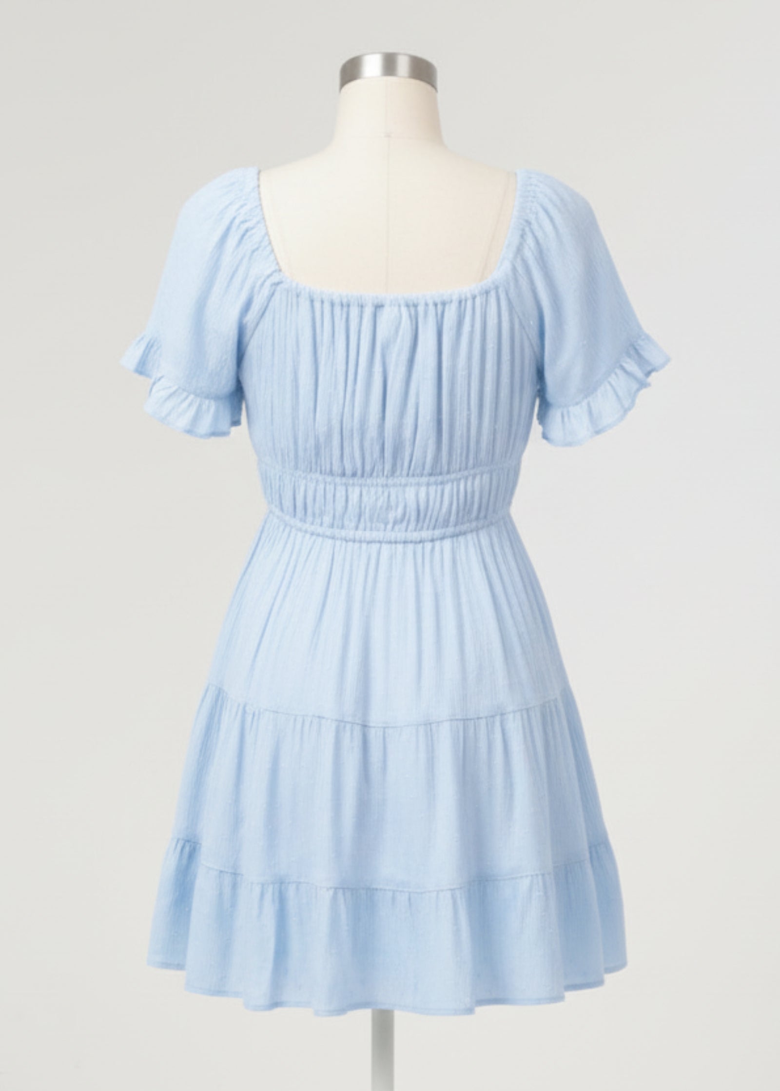 Woman wearing a light blue dress with ruffled sleeves and tiered skirt on a plain background