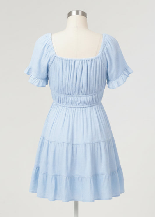 Woman wearing a light blue dress with ruffled sleeves and tiered skirt on a plain background
