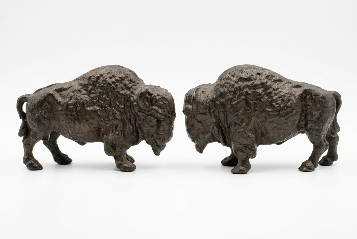 Two charcoal-black cast iron buffalo door stops facing each other on a white background