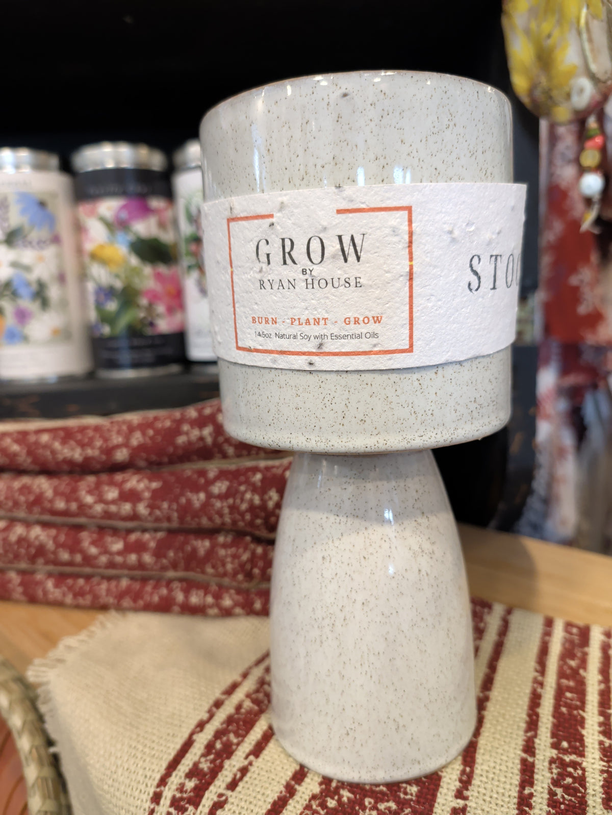 Ryan House Stockyards Candle with GROW label and speckled ivory pedestal base on a red-striped textile⠋

