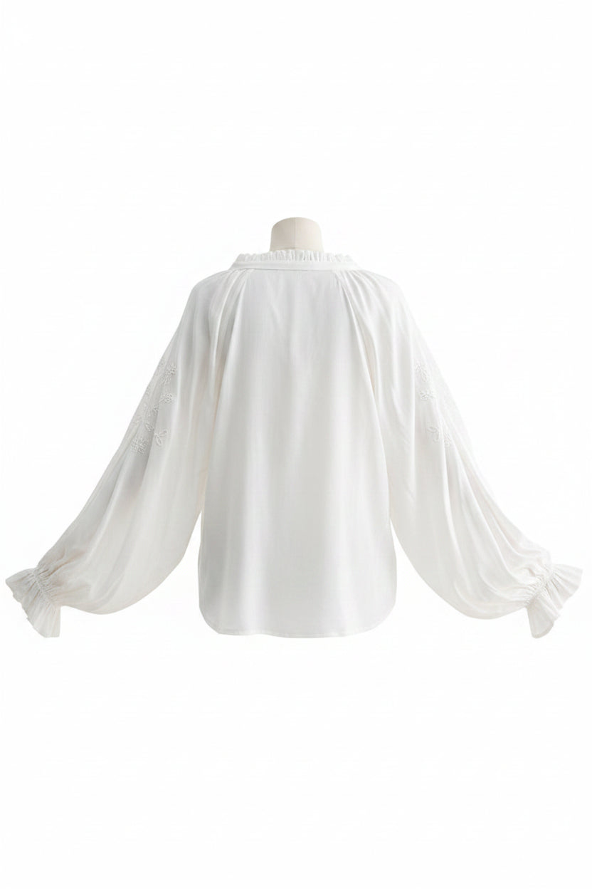 Woman wearing a white blouse with sheer sleeves and blue jeans on a white background