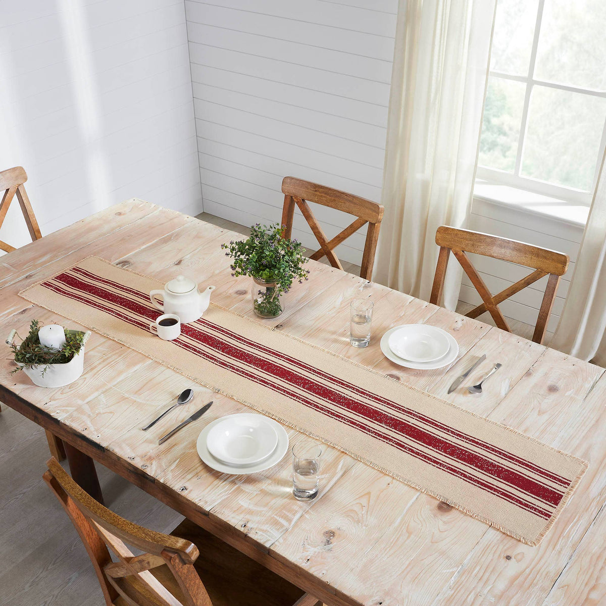 Cream cotton burlap table runner with distressed red stripes and fringed edges styled on a wooden dining table.