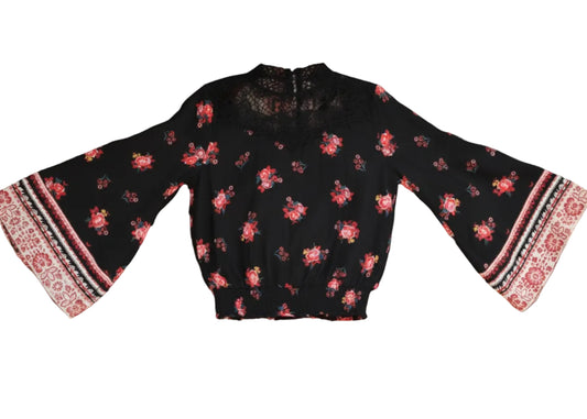 Woman wearing a black floral blouse with red and white accents against a rustic wooden background