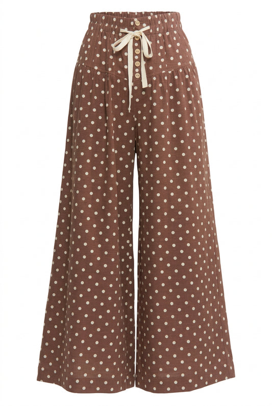Brown wide leg pants with cream polka dots, an elastic waistband, cream tie, and front button detail.