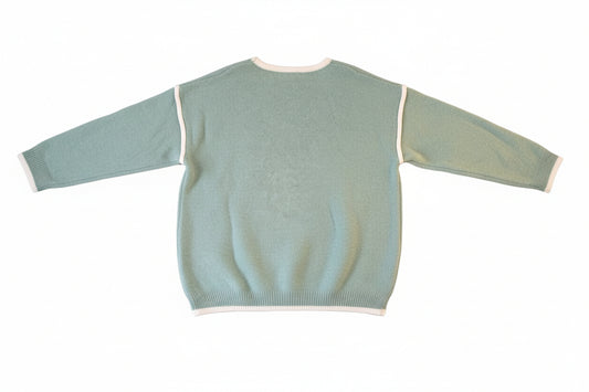 Green sweater with white trim on a wooden surface