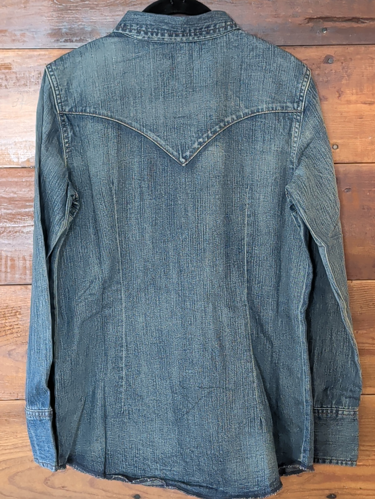 Back of the Wrangler women’s blue denim shirt showing the pointed Western yoke, long sleeves and curved hem.