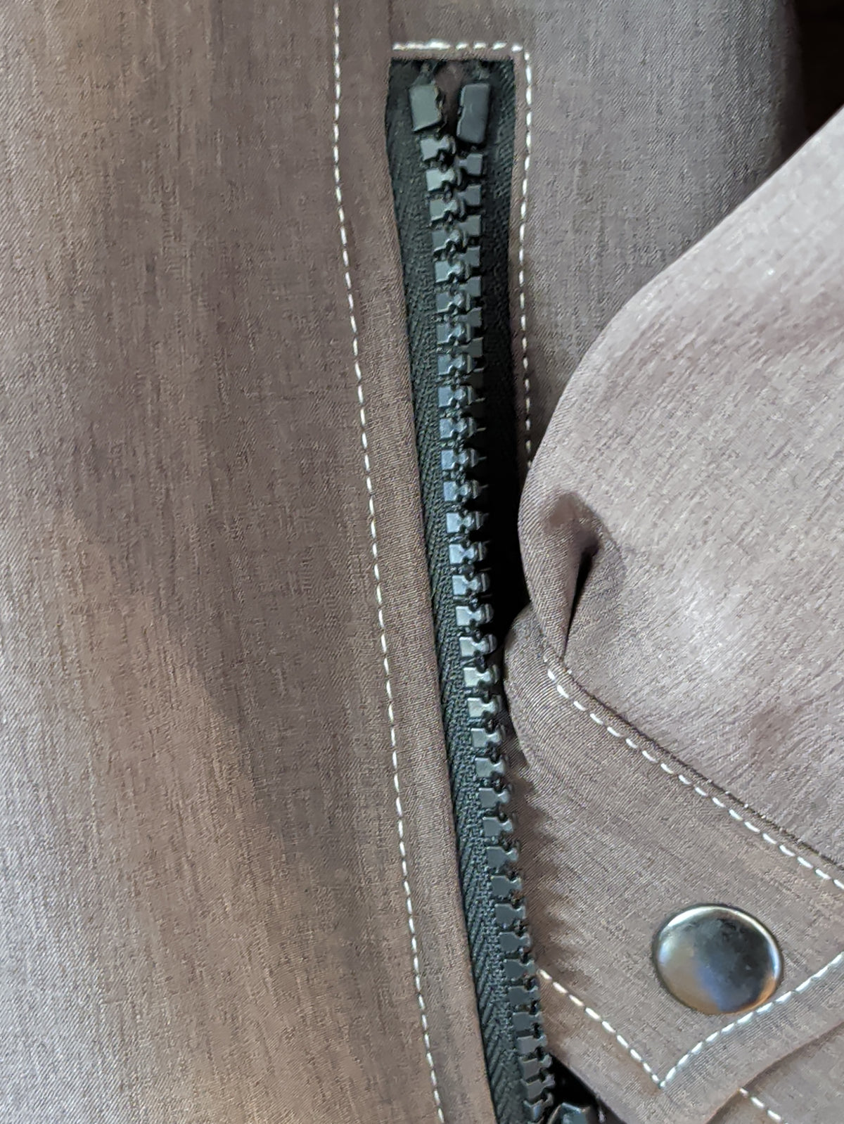 Close-up of the brown softshell jacket showing a zippered pocket, snap-tab cuff, and contrast stitching