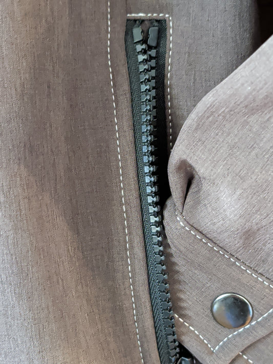 Close-up of the brown softshell jacket showing a zippered pocket, snap-tab cuff, and contrast stitching