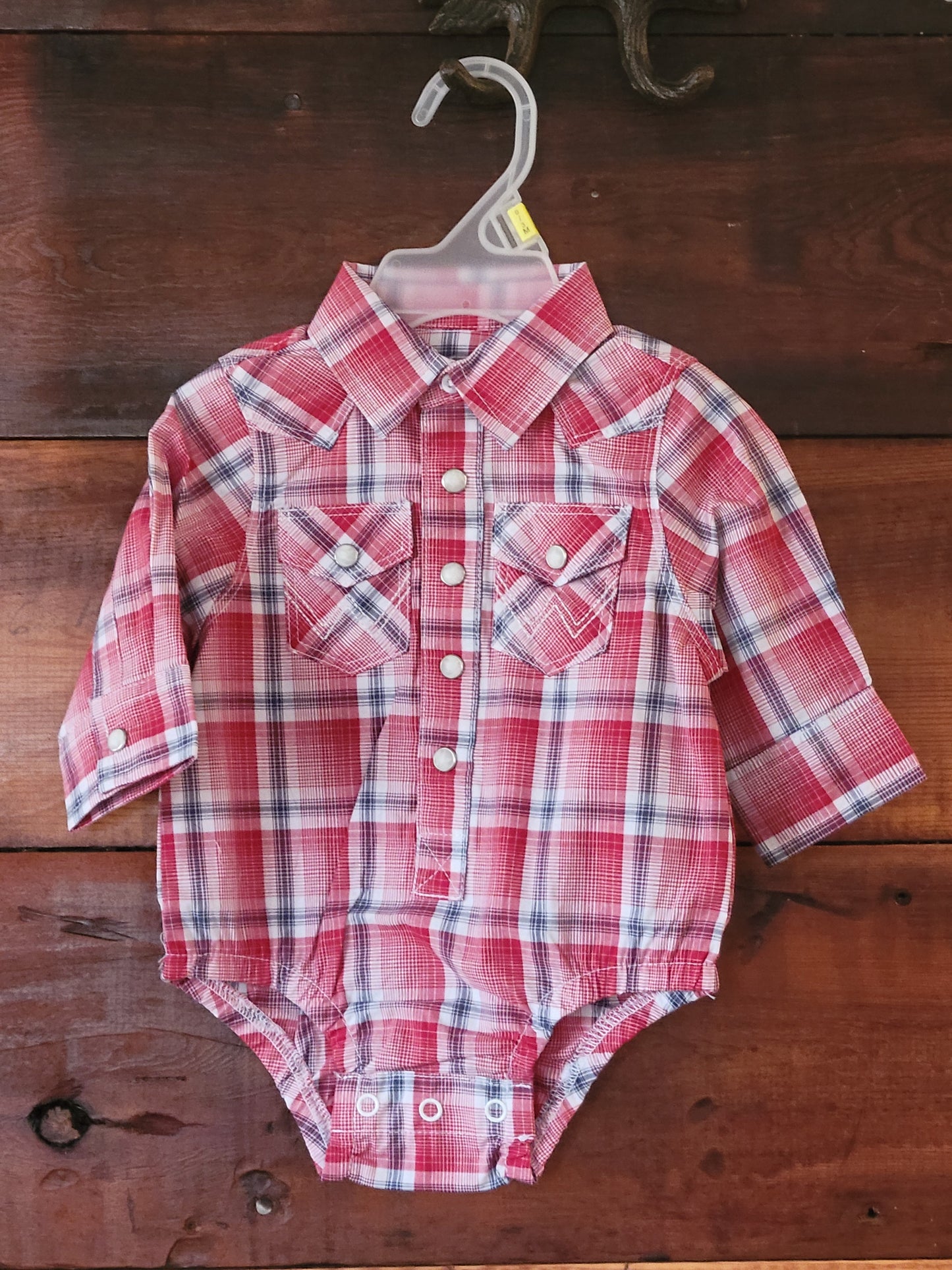 Red and white plaid baby romper on a wooden surface
