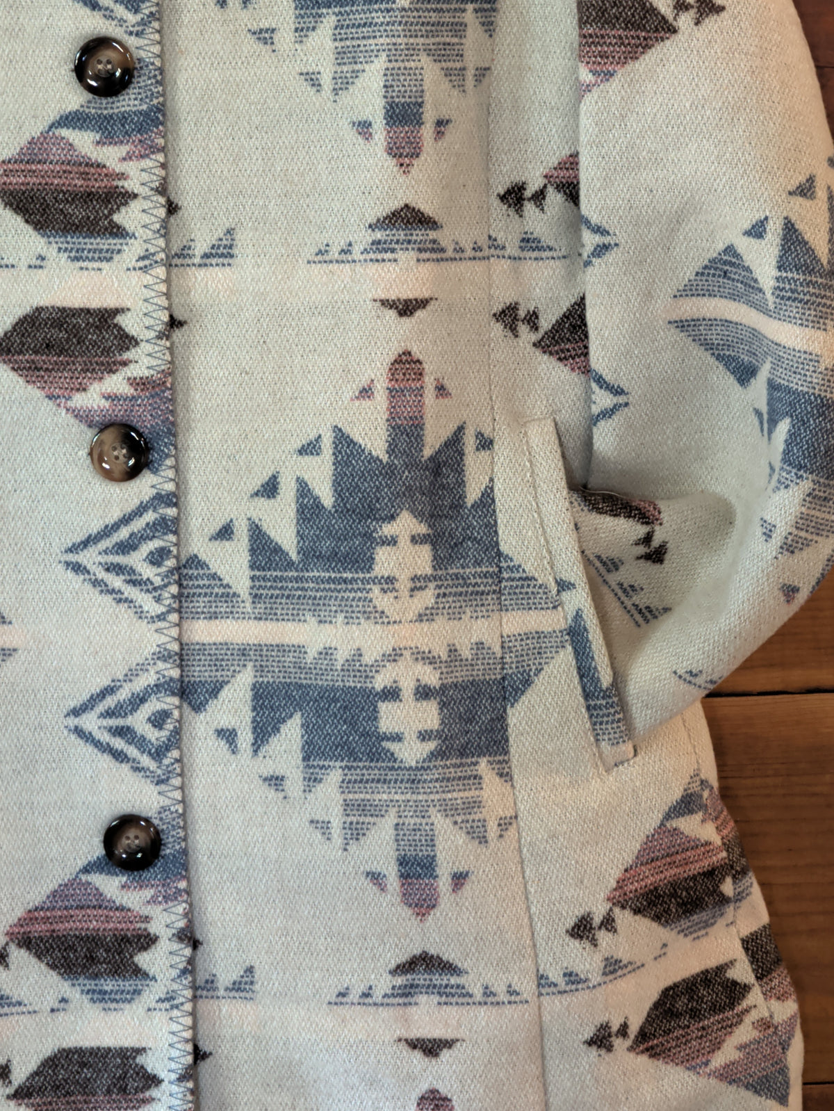 Close-up of the Southwestern print coat showing a front welt pocket and blue and mauve geometric pattern