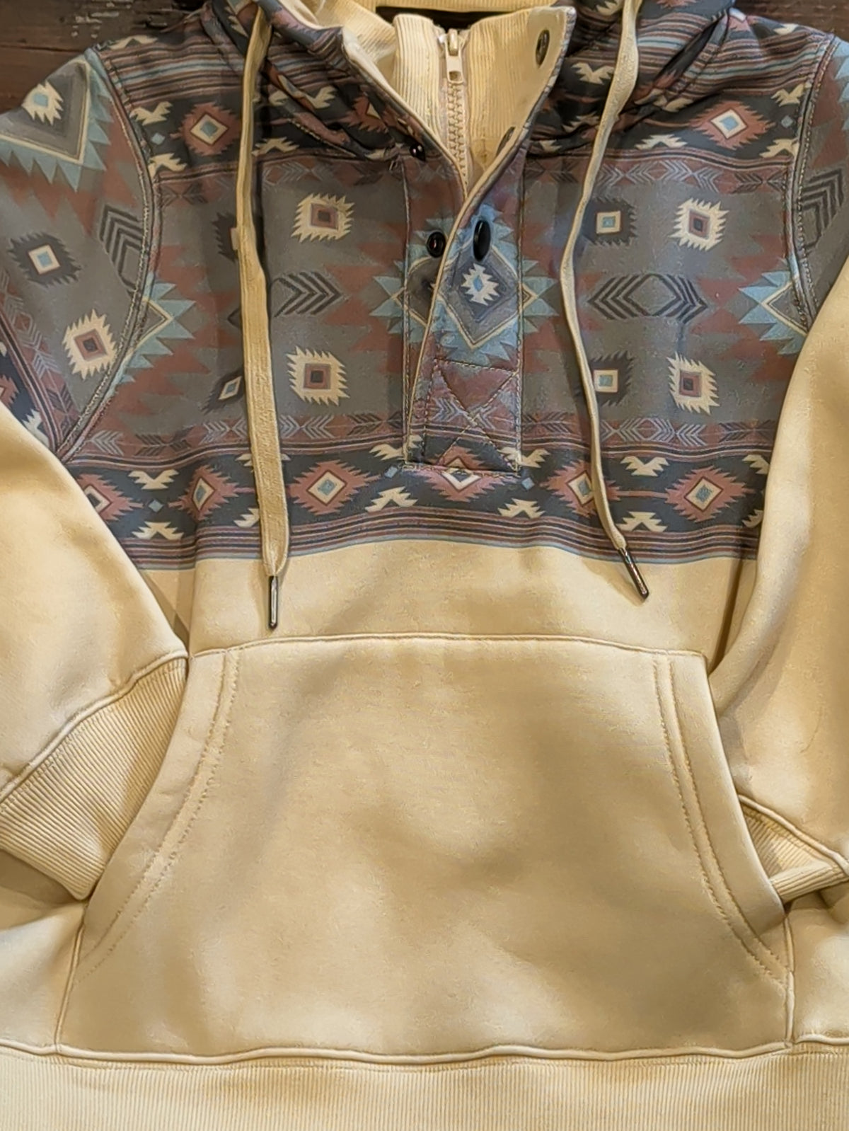 Front detail of the cream fleece hoodie showing the kangaroo pocket, ribbed hem, and contrasting Southwestern print chest