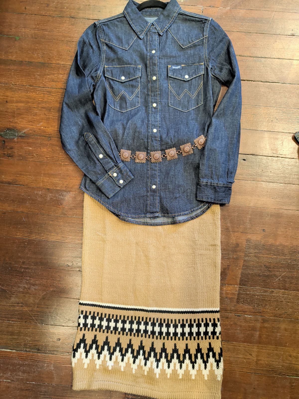 Light brown knit skirt with black and cream Fair Isle pattern near the hem, styled with a denim shirt and decorative belt.