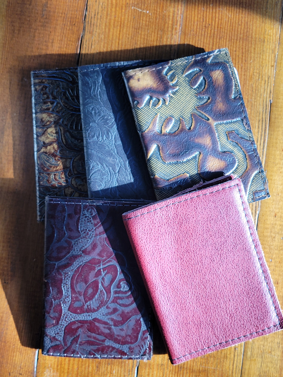 Pocket-size leather journals in assorted colors with textured and embossed cover designs on a wooden surface