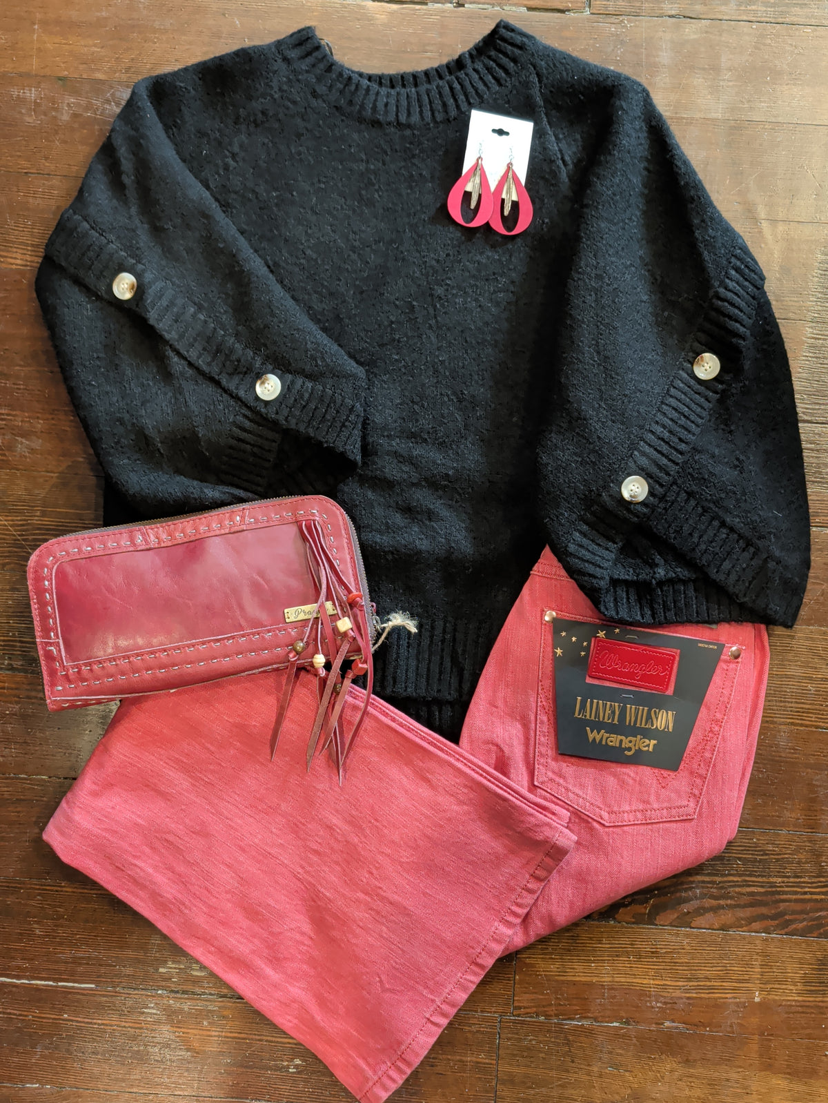 Black button-sleeve knit pullover styled flat with Red Wrangler jeans,red teardrop earrings, and a red zip wallet with wrist strap.