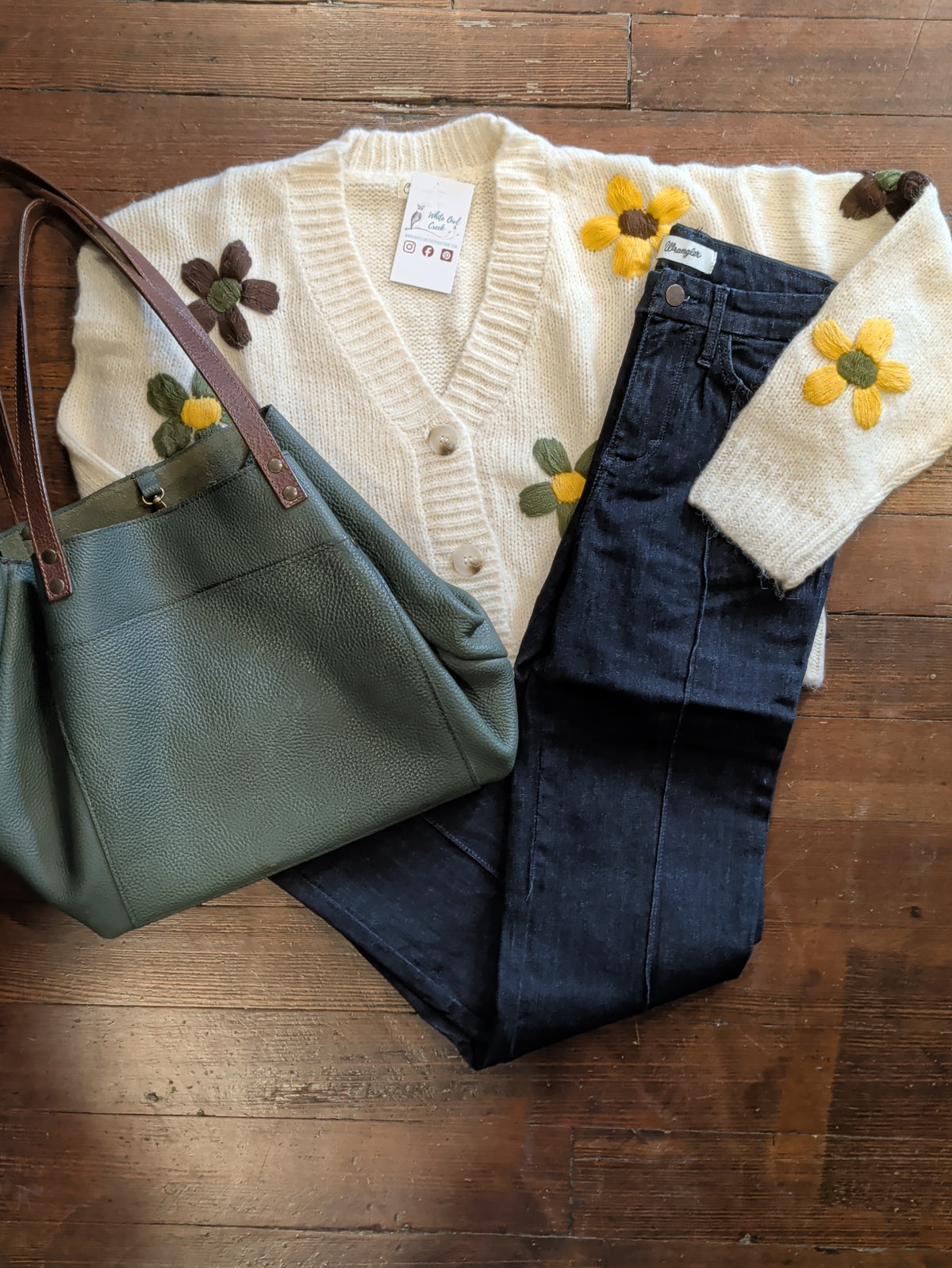 Folded Wrangler Bespoke Camryn pintuck jeans styled with a cream floral cardigan and green tote.
