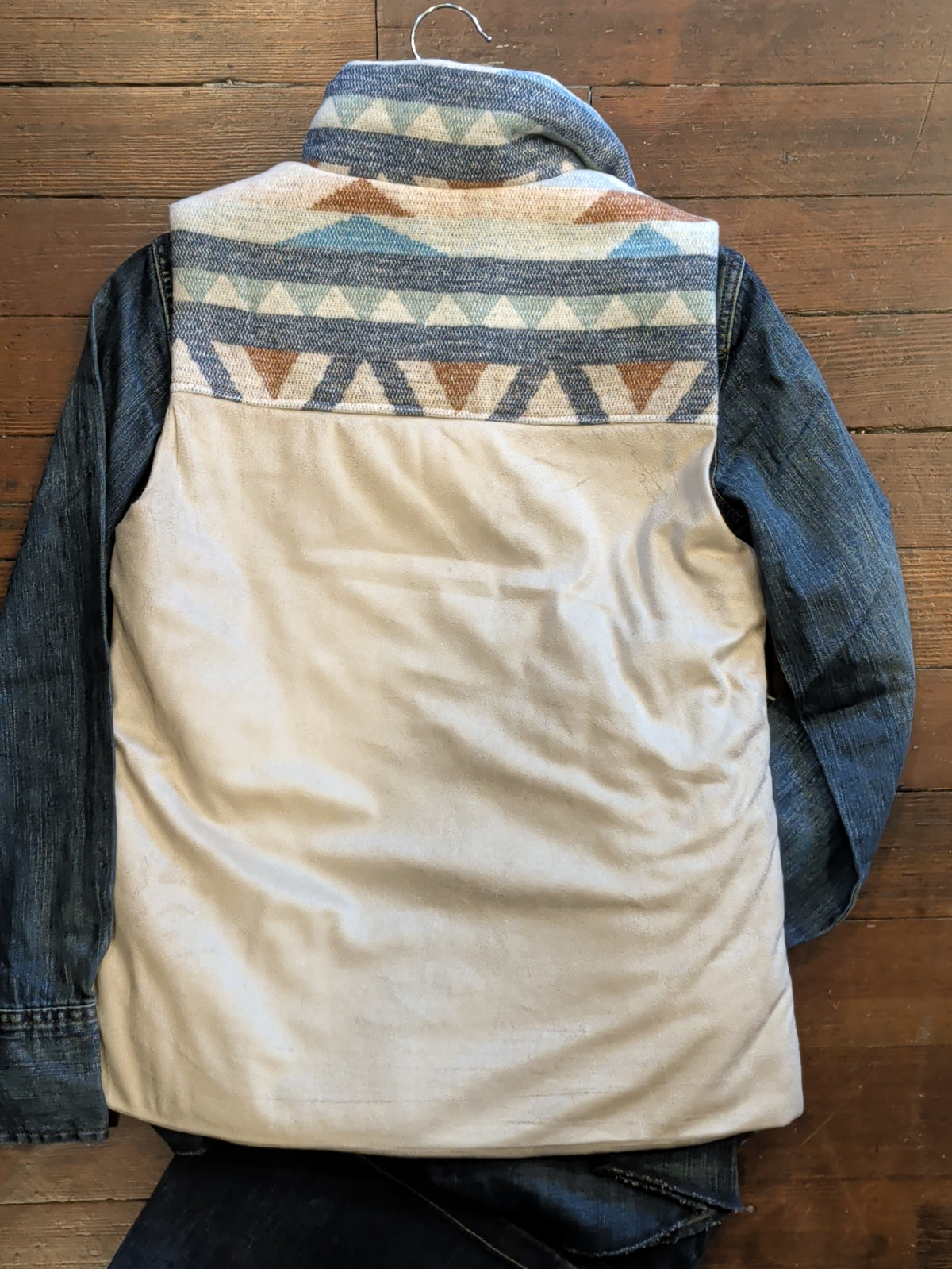 Back of cream vest with blue, turquoise, and brown geometric shoulder yoke, layered over a denim shirt.