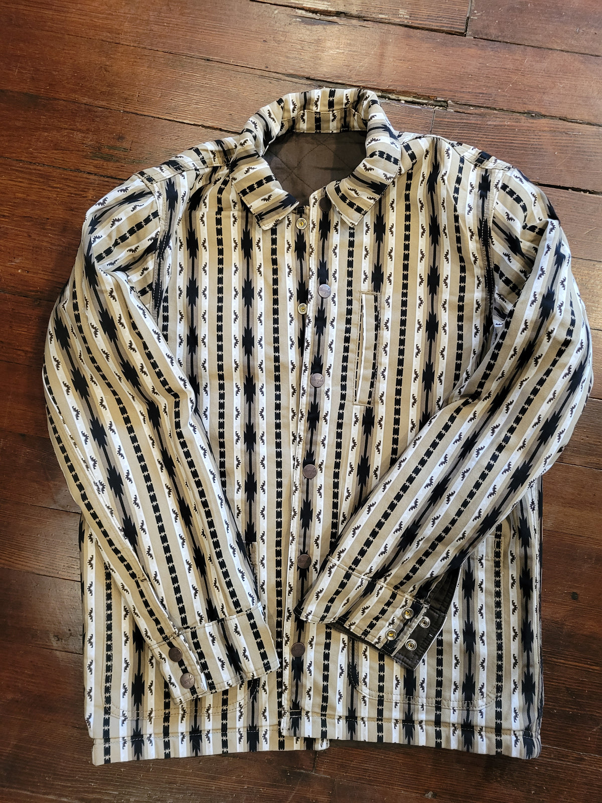 A jacket with button-up shirt with a beige, black, and white geometric pattern, laid flat on a dark wood floor.