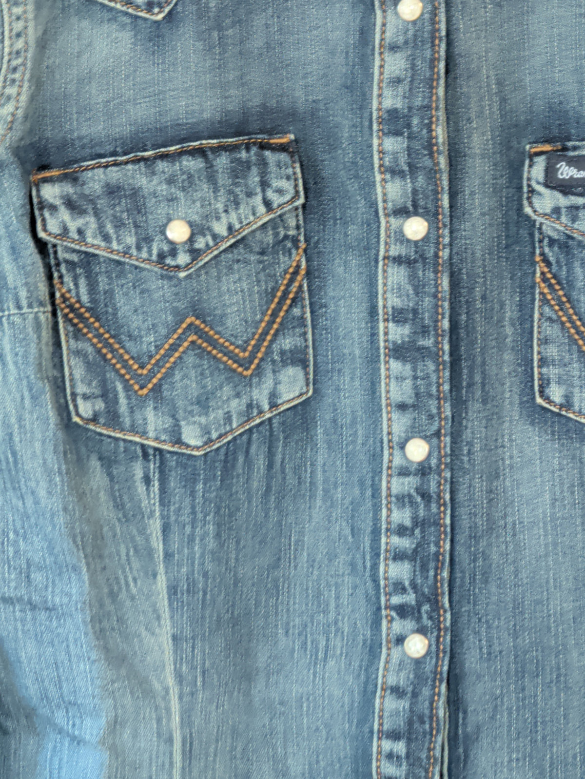 Close-up of the Wrangler denim shirt’s snap-flap chest pocket with contrast W stitching and snap-front closure.
