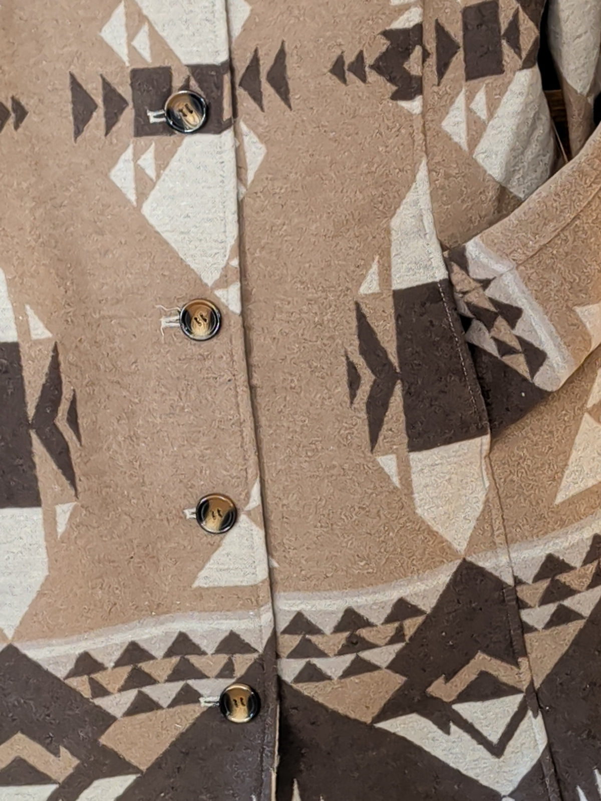  Close-up of the coat's brown buttons, front pocket, and cream, taupe, and brown geometric pattern.