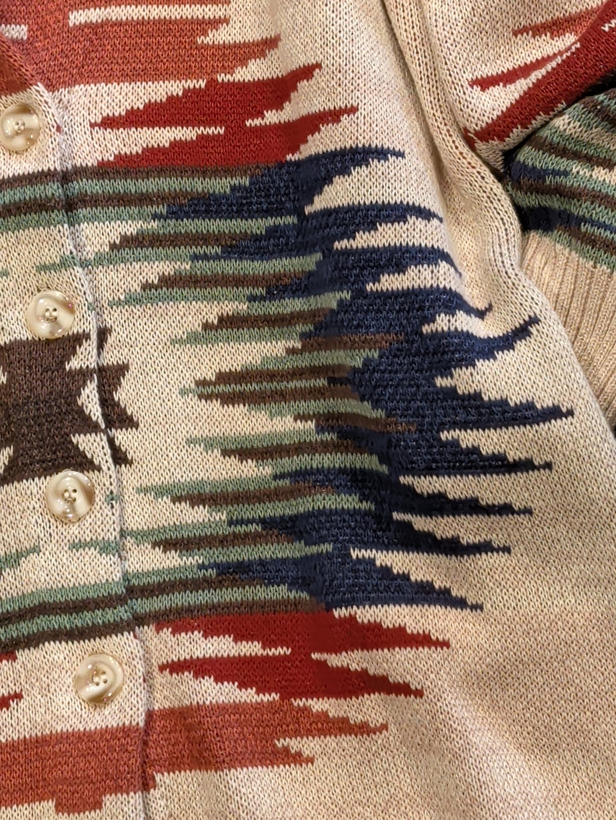Close-up of cream cardigan showing Southwestern knit pattern in rust, navy, sage, and brown with cream front buttons.